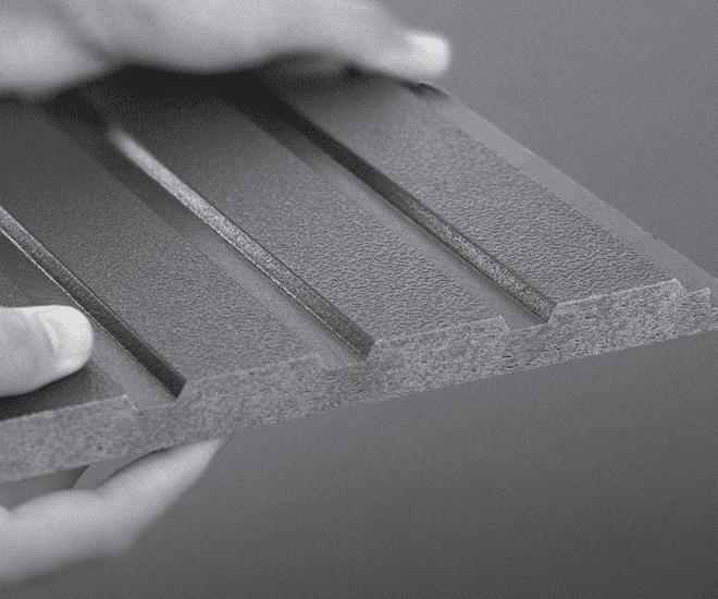A close-up of two hands holding a rectangular, textured panel with three parallel grooves running lengthwise. The panel appears to be made of a dense, possibly synthetic material.