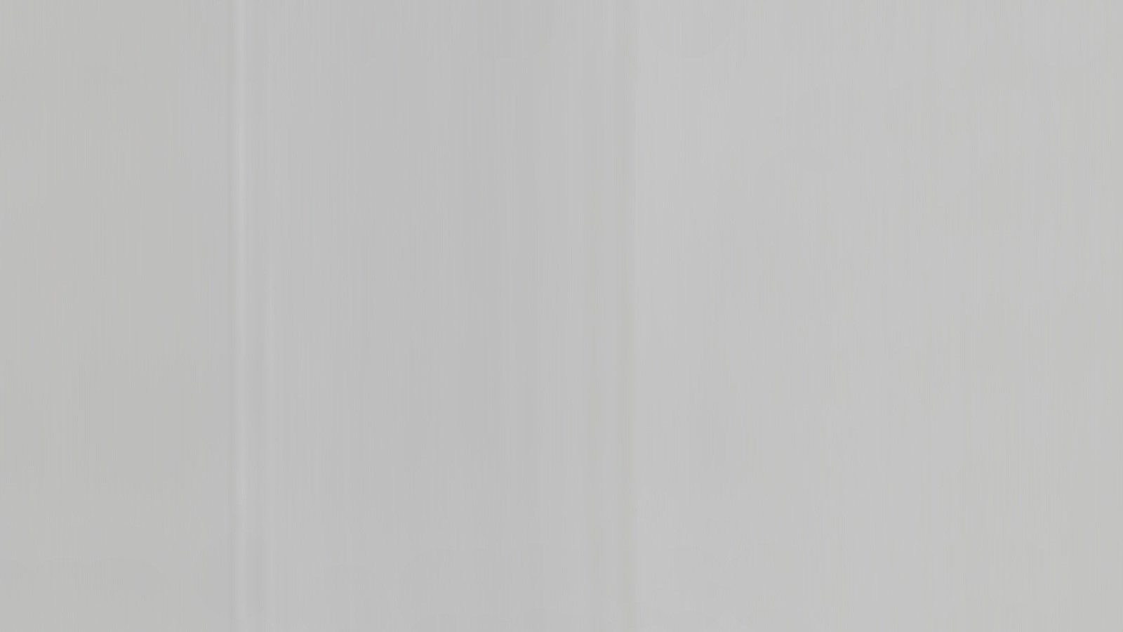 A close-up view of a smooth, light gray, plain wall with subtle vertical lines running down its surface.