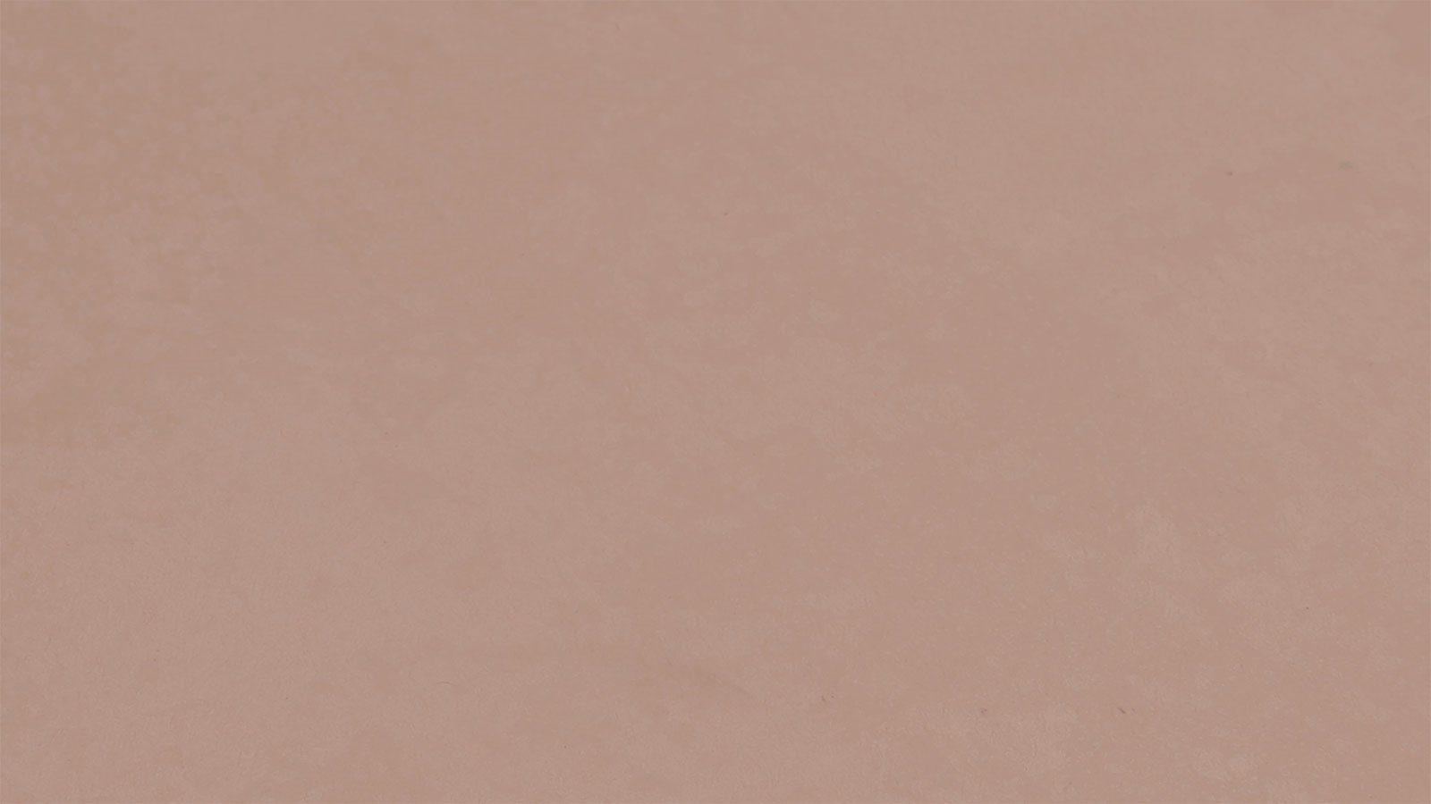 A close-up view of a light peach-colored surface with a slightly mottled texture. The surface is flat and uniformly colored, with subtle variations in shade creating a soft, abstract pattern.