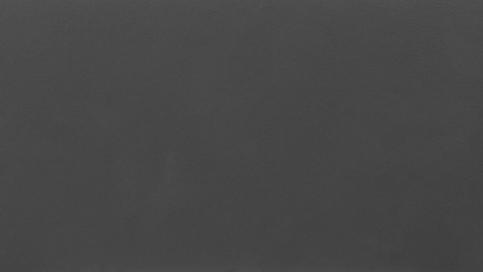 A close-up of a dark gray, textured surface. The material appears smooth and slightly matte with a uniform color throughout. There are no visible patterns, markings, or objects, just an expanse of the dark gray texture.